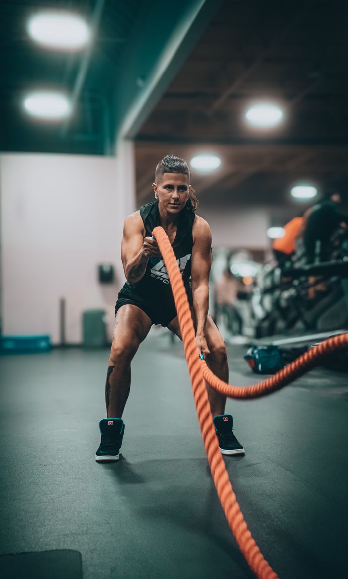 social-feed-img-03 Athletic person performing an intense battle rope exercise in a modern gym setting.